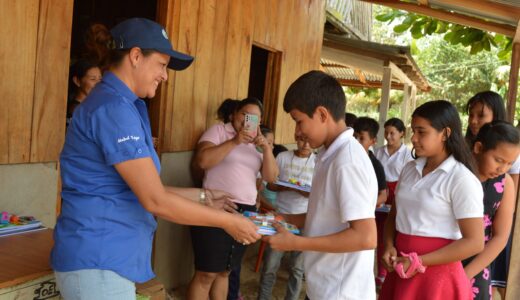Mabel Lazo Quino, responsable de Gestión Social de MLR Forestal, entrega su paquete de útiles escolares a un estudiante de la escuela Nueva Esperanza en la comunidad Bethel II.